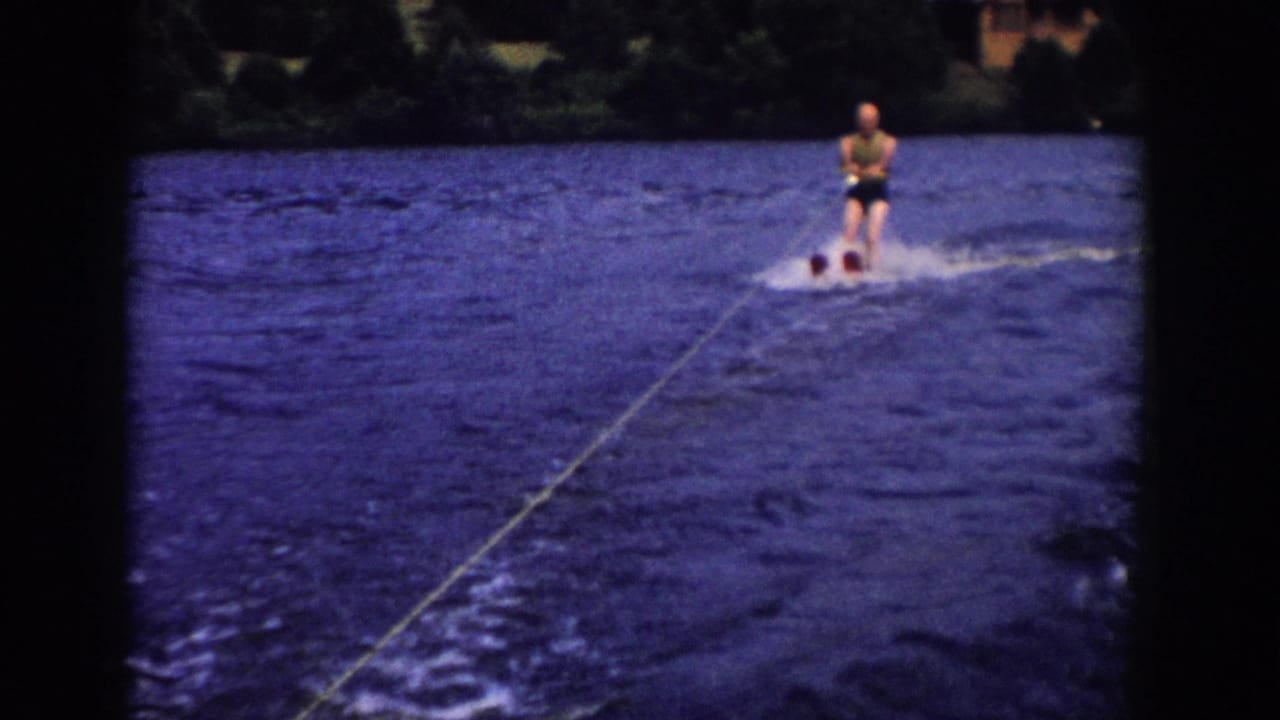 Water skier follows a tow rope across a blue lake with trees on the far shore.
