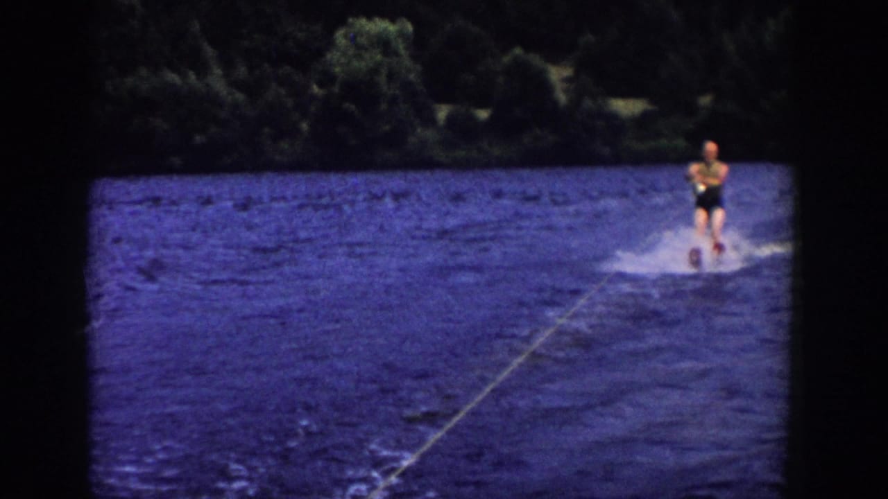 Water skier appears farther right on the lake while the tow rope cuts across the water.