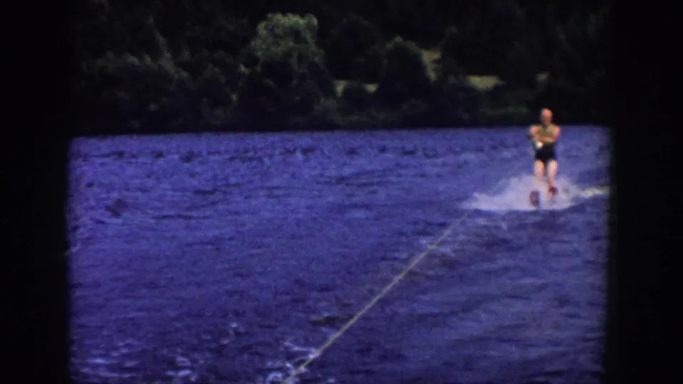 Water skier in a dark swimsuit moves across a Wisconsin lake in soft 8mm footage from 1958.