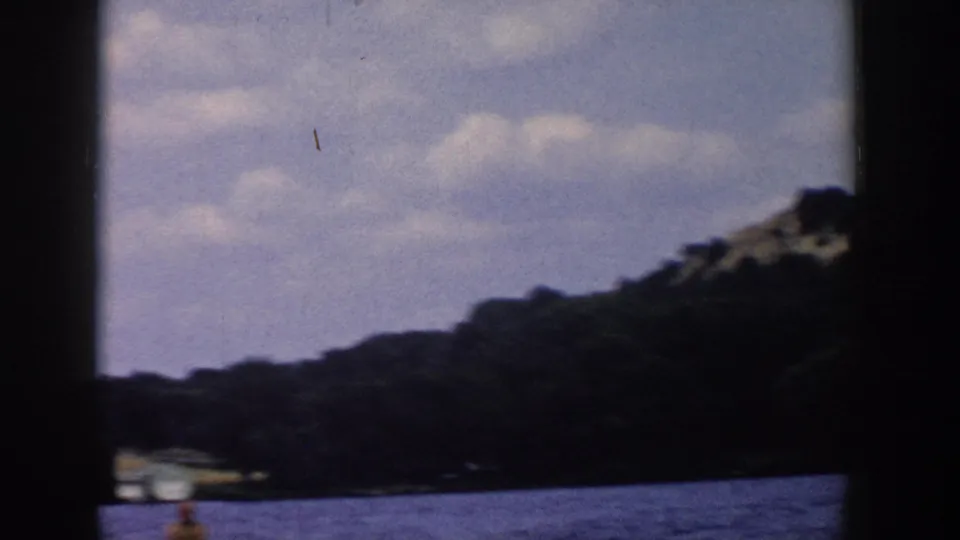 Wisconsin lake scene from 1958 home-movie footage, with wooded shore, cloudy sky, and the skier partly visible near the lower edge.
