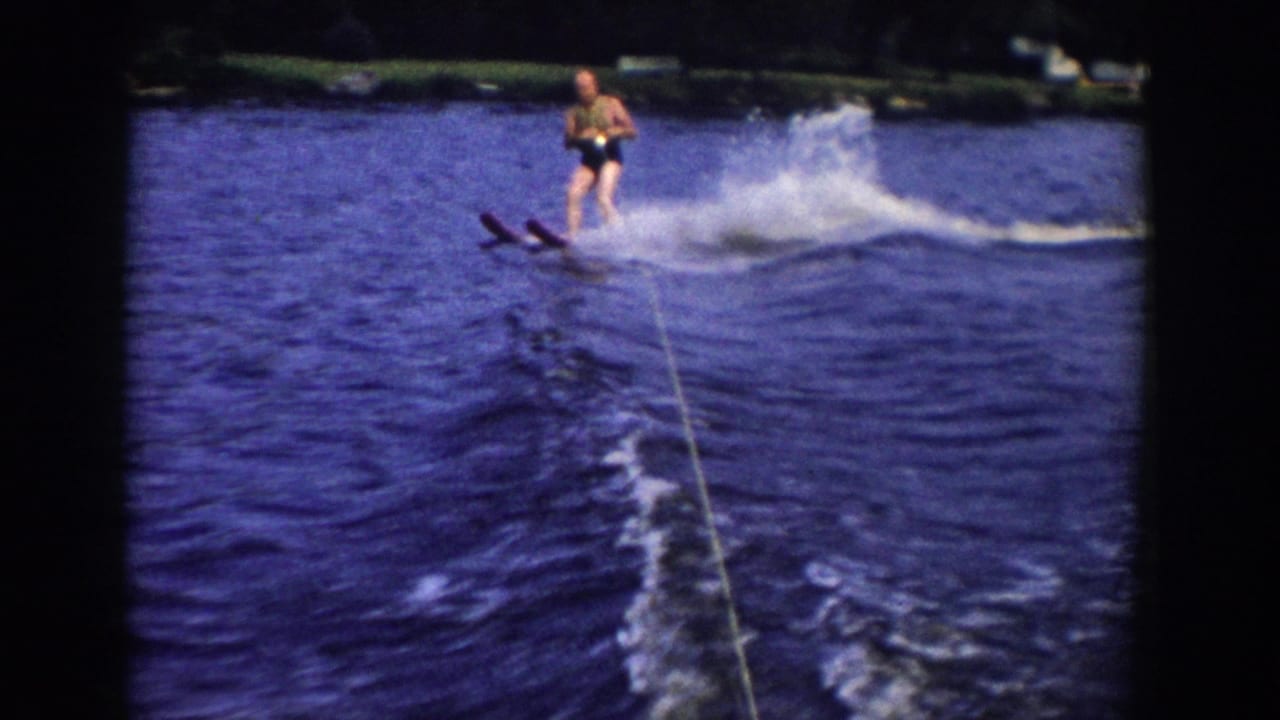 A water skier in swimsuit and life vest leans near the wake, with spray and the tow rope visible in the 1958 Wisconsin home movie.