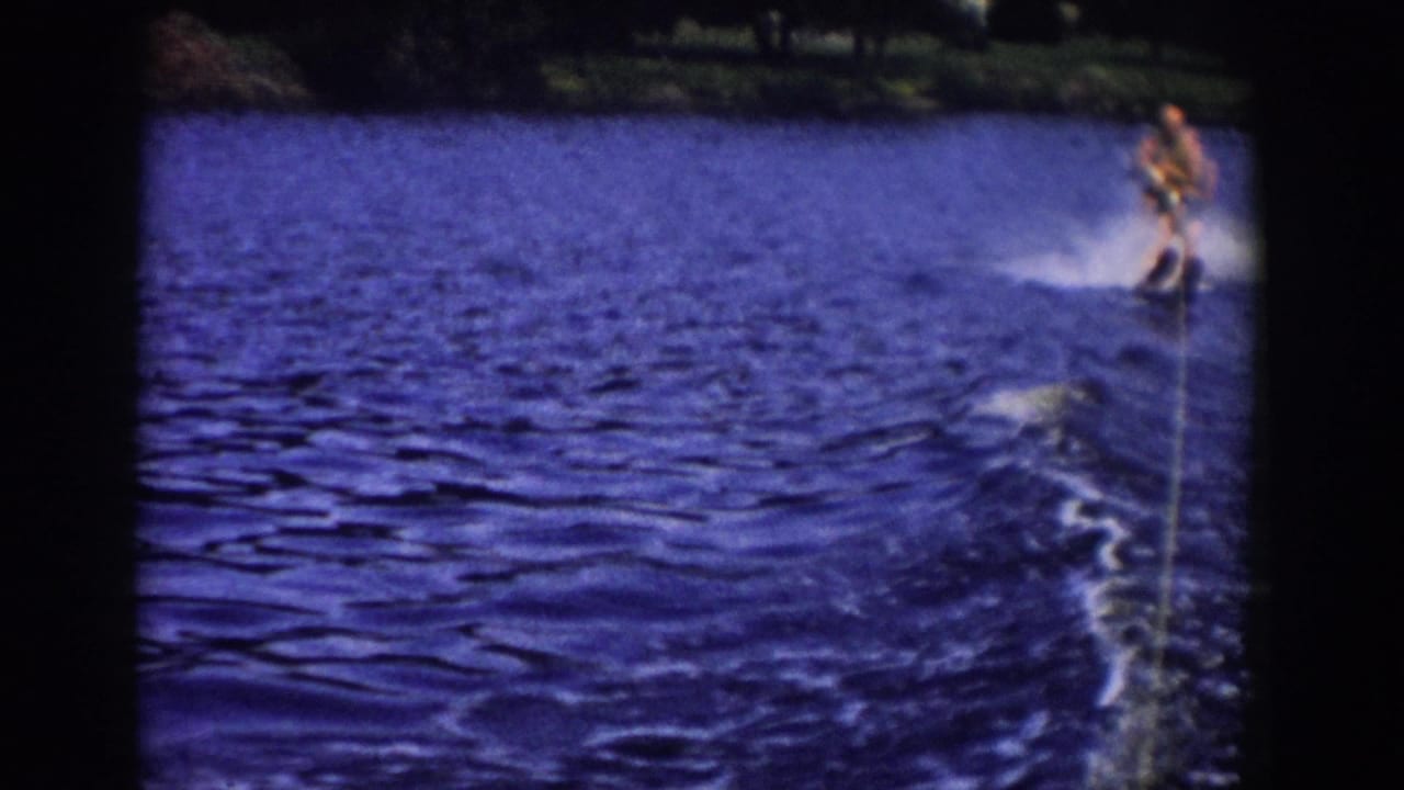 Water skier near the right side of a blue lake with a tow rope leading toward the camera.