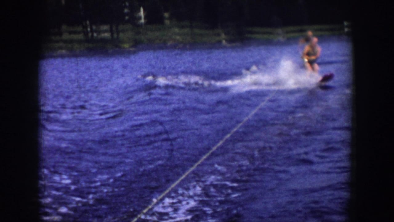 Water skier at upper right throws spray while crossing the lake behind a visible tow rope.