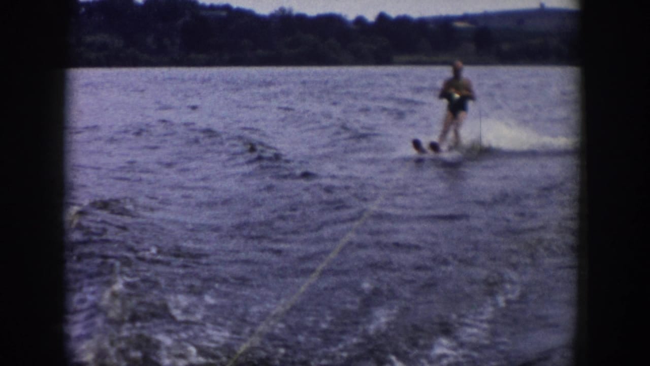 1958 Wisconsin home-movie frame of a water-skier near the edge of the shot, pulled across the lake as spray rises behind the skis.