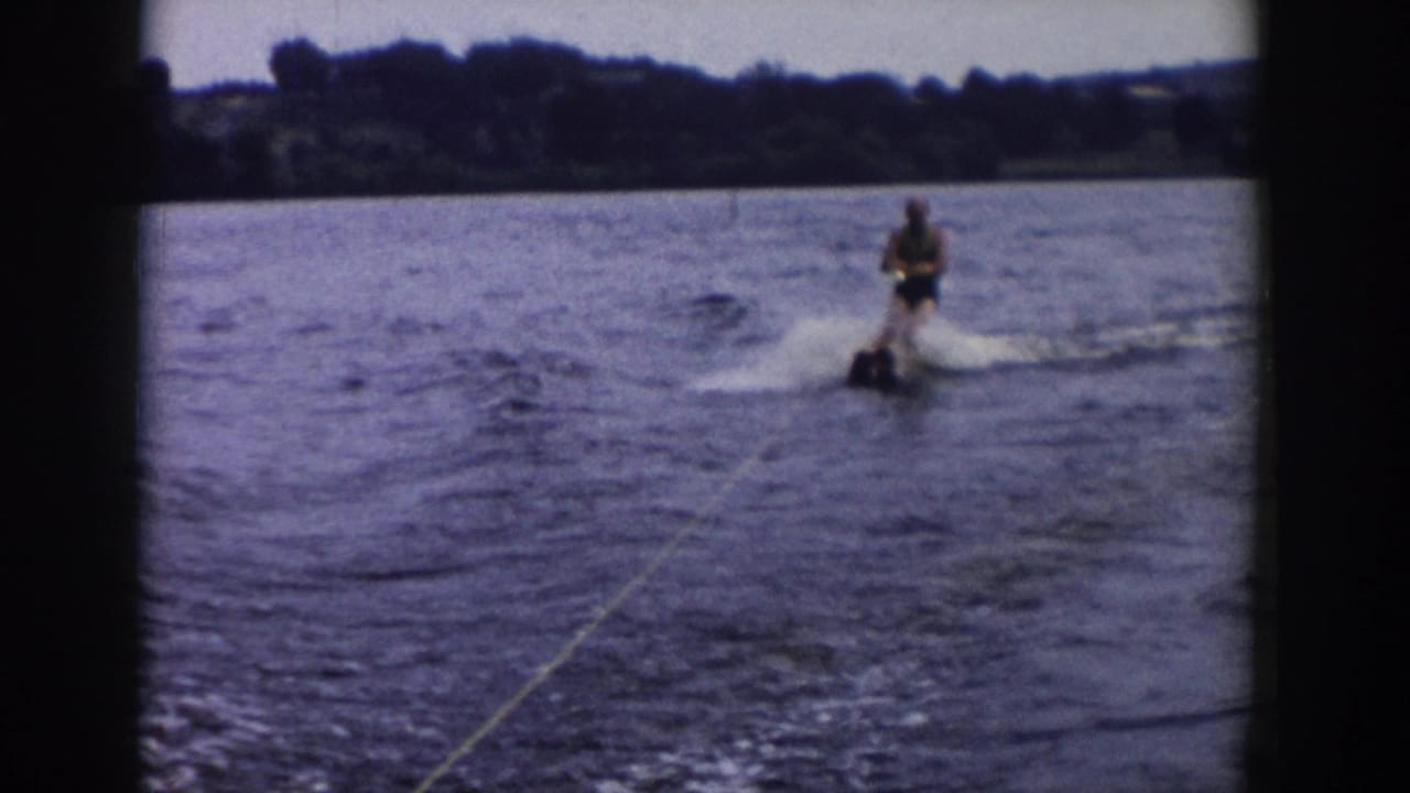 Water skier rides behind a boat on a lake with a tow rope and tree-lined shore.