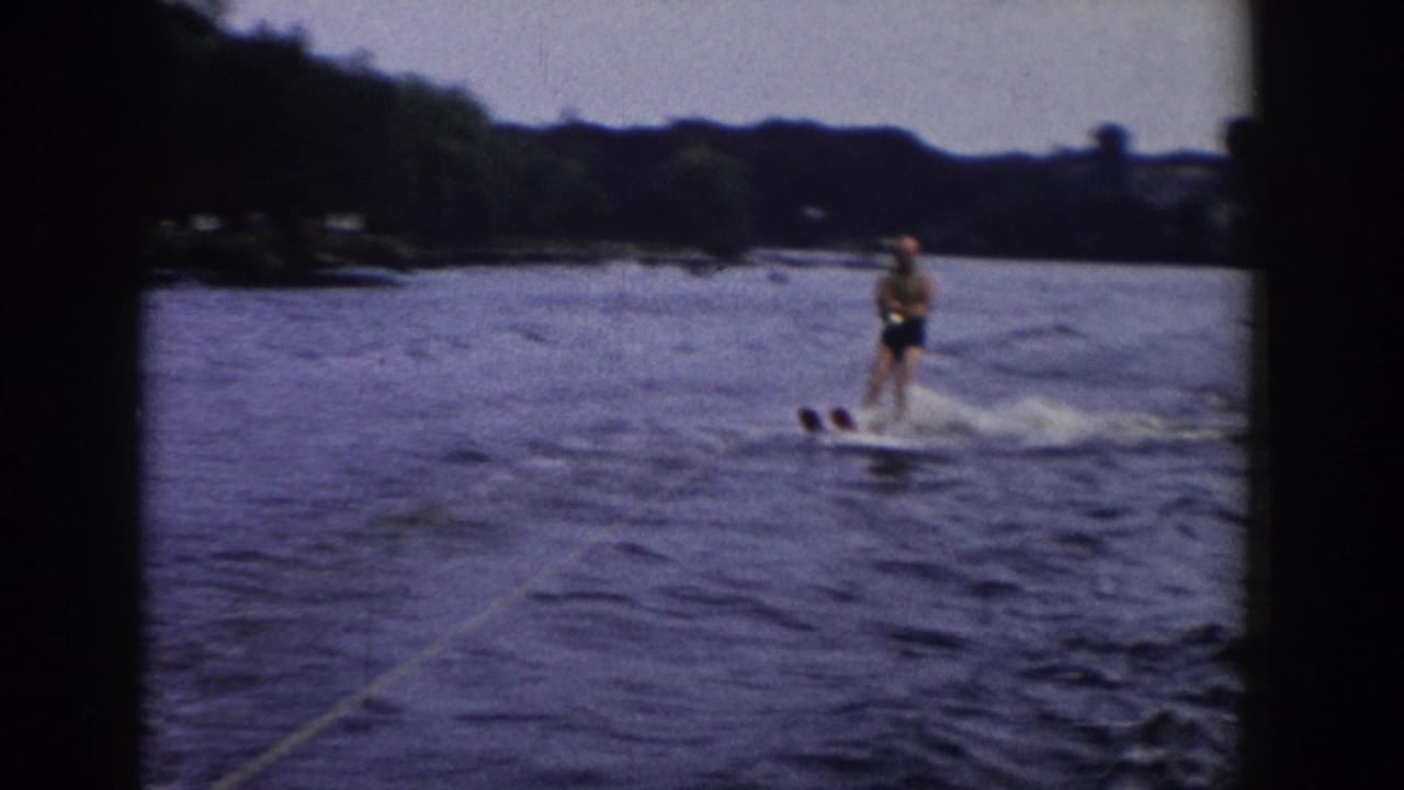 Final 1958 Wisconsin 8mm frame showing the adult skier moving right across the lake, with tow rope, wake, and dark film borders visible.