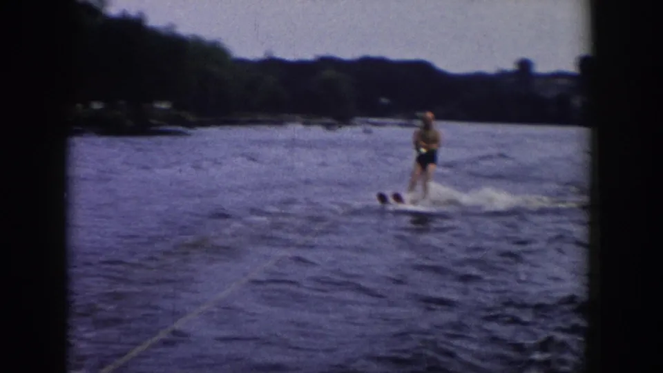 Final 1958 Wisconsin 8mm frame showing the adult skier moving right across the lake, with tow rope, wake, and dark film borders visible.