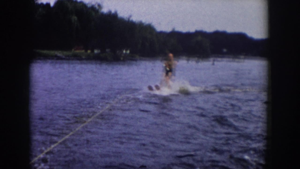 Water skier being towed across a lake with a wooded shoreline in the distance.