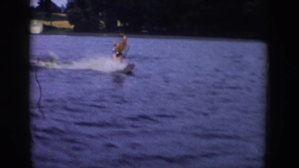 1958 Wisconsin home-movie frame of a man water skiing on a lake with spray and trees behind him.