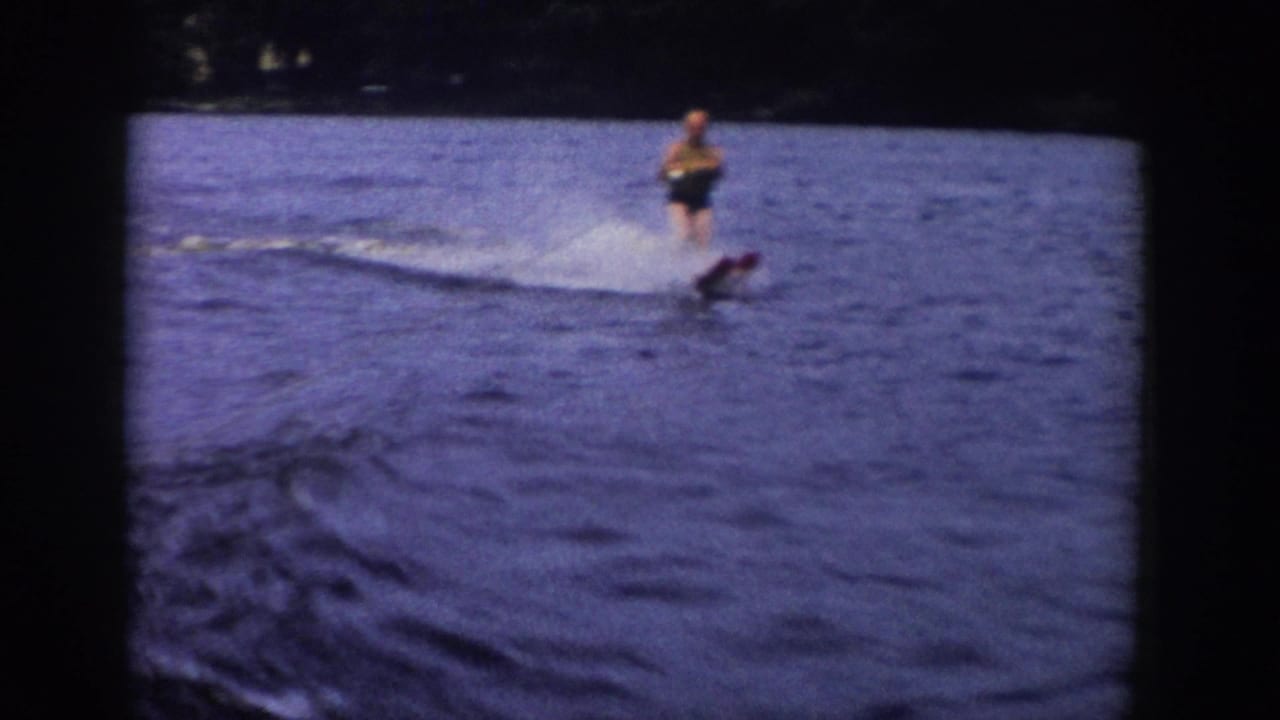 1958 Wisconsin home-movie frame of a man water skiing as the wake curves across the blue-purple lake surface.