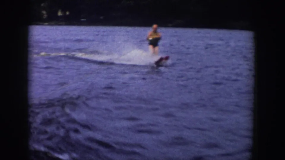 1958 Wisconsin home-movie frame of a man water skiing as the wake curves across the blue-purple lake surface.