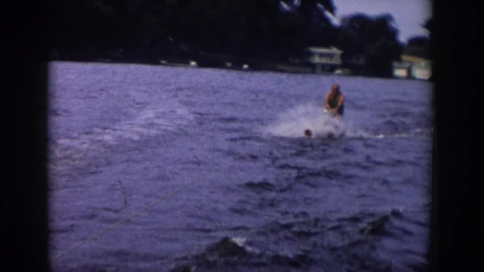 A soft 8mm frame from 1958 Wisconsin shows the skier amid spray, with the lake and distant trees filling most of the view.