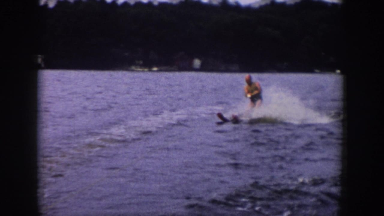 1958 Wisconsin 8mm frame showing a man water skiing across a lake, with spray behind him and dark film borders around the scene.