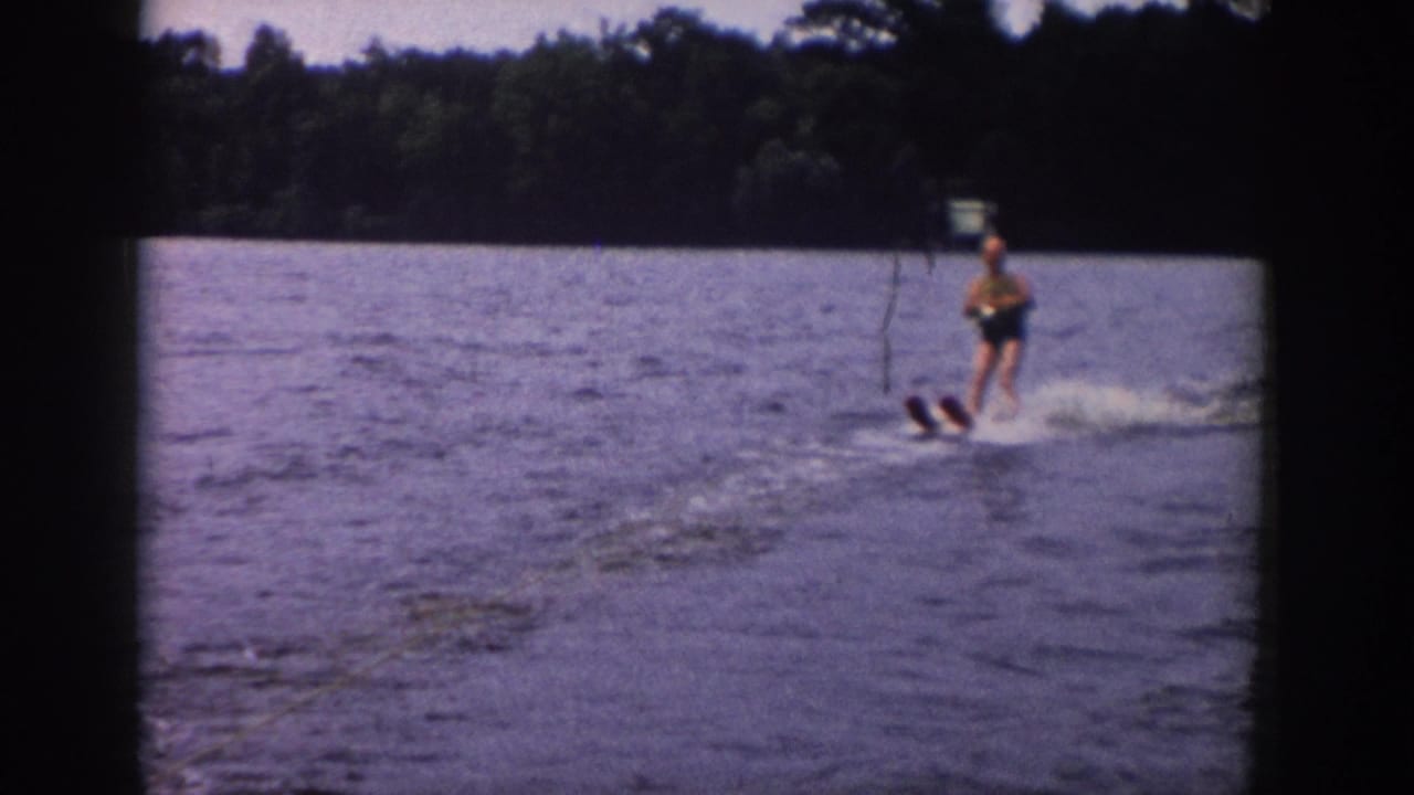 The skier stands upright on twin skis, holding a tow rope as the lake surface breaks into a white wake behind him.