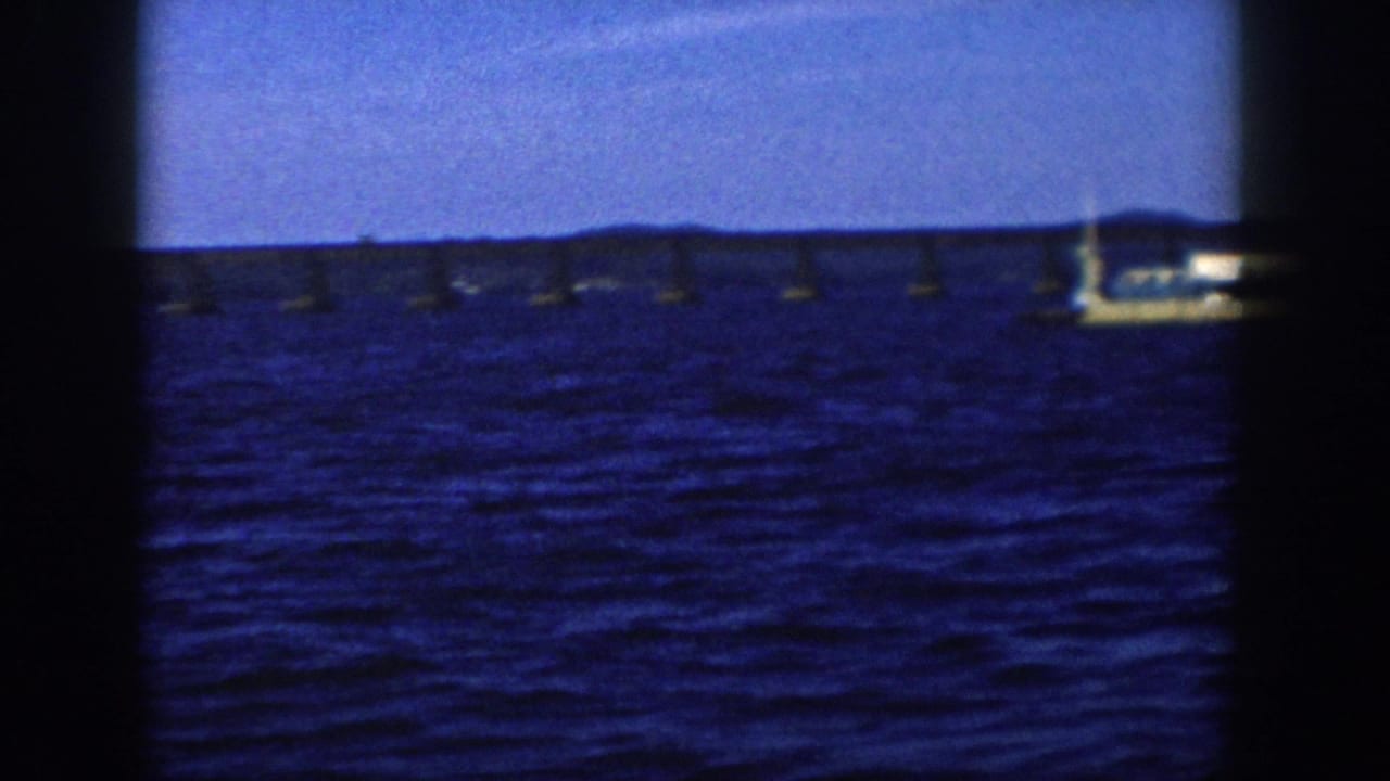 The 1958 Wisconsin barge scene ends as the vessel moves partly out of frame beside a long bridge over the lake.
