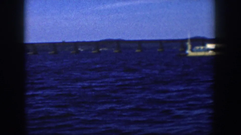 The 1958 Wisconsin barge scene ends as the vessel moves partly out of frame beside a long bridge over the lake.