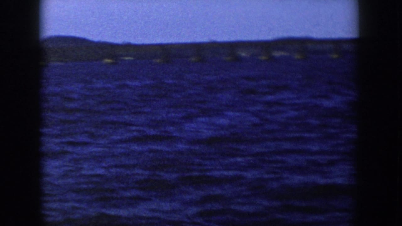 1958 Wisconsin 8mm frame showing choppy blue water, dark shoreline, and soft sky through rounded film borders.