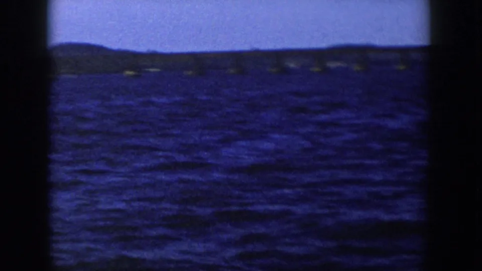 1958 Wisconsin 8mm frame showing choppy blue water, dark shoreline, and soft sky through rounded film borders.