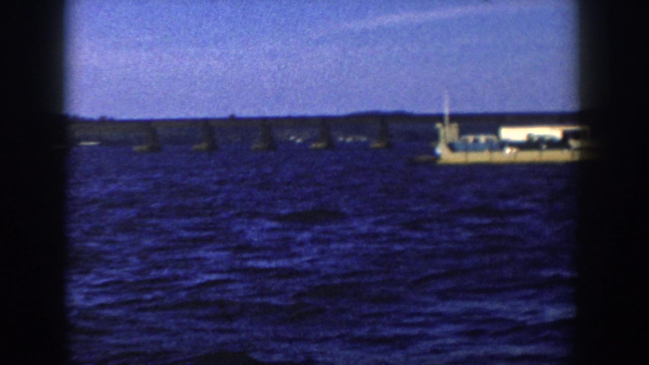 1958 Wisconsin 8mm frame with a light-colored ship entering the view across choppy blue water, backed by buoys and low shoreline.