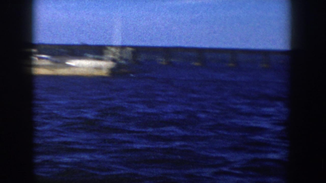 1958 Wisconsin 8mm frame with the vessel mostly leaving view, open water, distant bridge or shoreline, and heavy dark film borders.