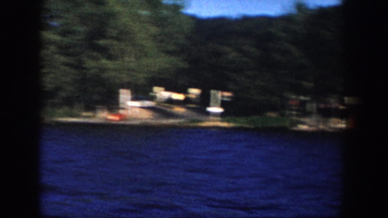 1958 Wisconsin 8mm frame showing choppy blue lake water and a distant wooded shoreline with small lakeside structures.