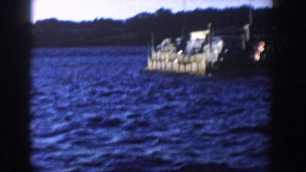 Vehicle-carrying boat near the right edge crossing choppy lake water.