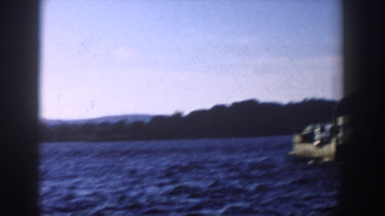 1958 Wisconsin 8mm frame of open lake water, distant wooded hills, and the edge of the vehicle-carrying boat leaving frame.