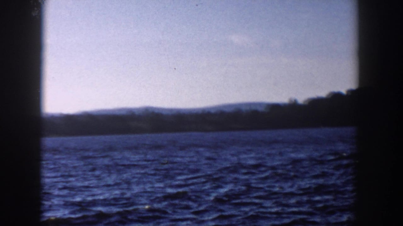1958 Wisconsin 8mm frame showing rippled water, a low wooded shore, and dark window-like framing in the foreground.