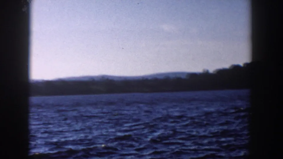 1958 Wisconsin 8mm frame showing rippled water, a low wooded shore, and dark window-like framing in the foreground.