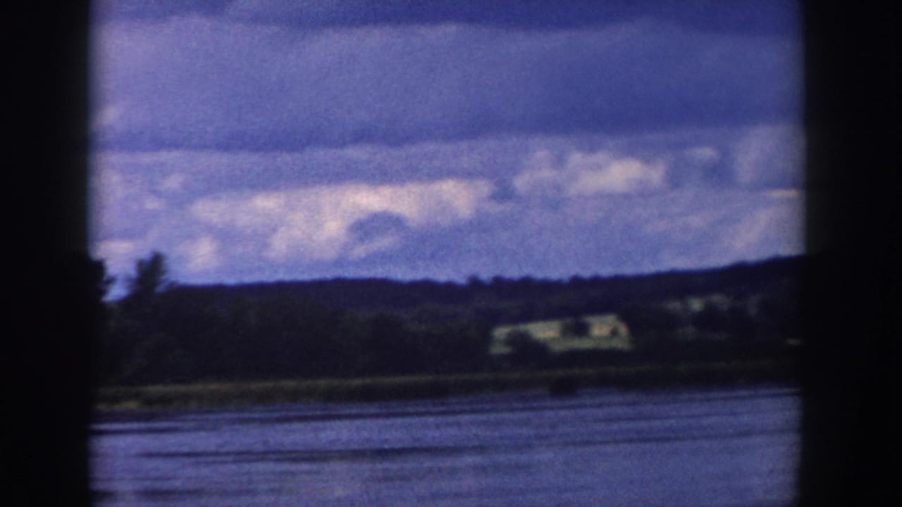 1958 Wisconsin lakeside panorama with blue-gray water, distant shoreline buildings, low hills, trees, and a broad cloudy sky.