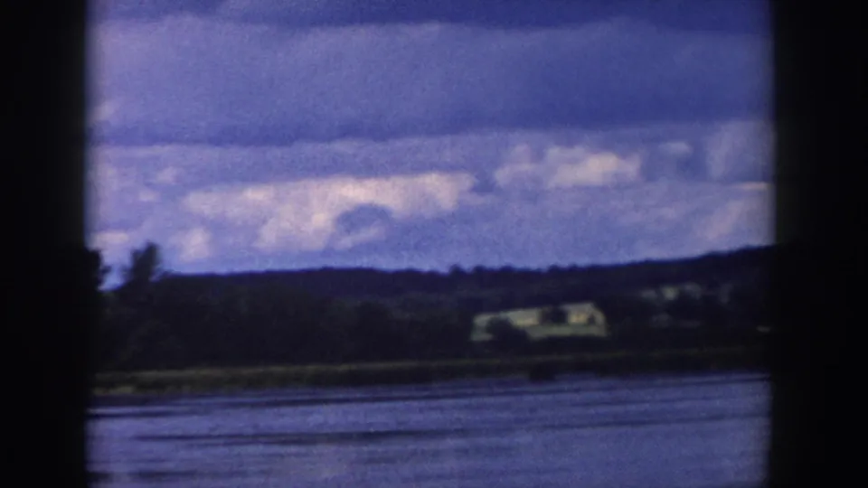 1958 Wisconsin lakeside panorama with blue-gray water, distant shoreline buildings, low hills, trees, and a broad cloudy sky.