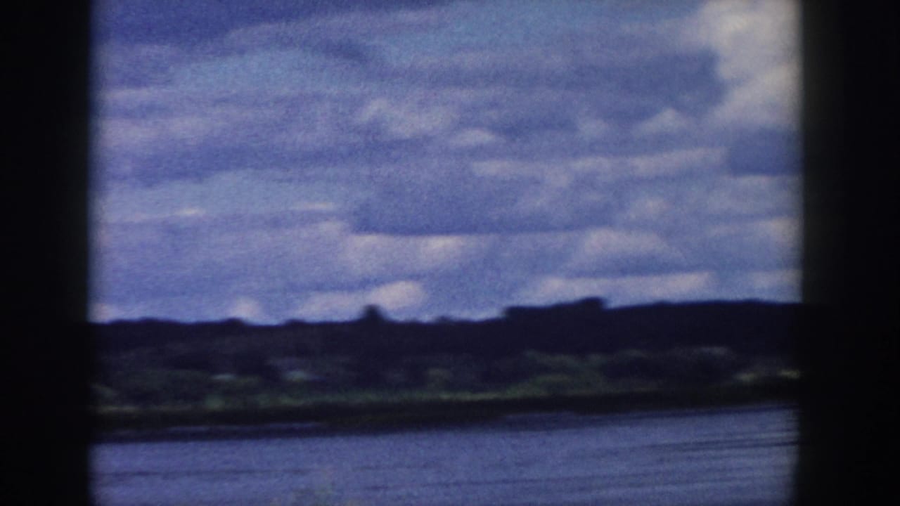 1958 Wisconsin 8mm frame showing open water, distant green hills, and a layered cloudy sky behind dark window-like framing.
