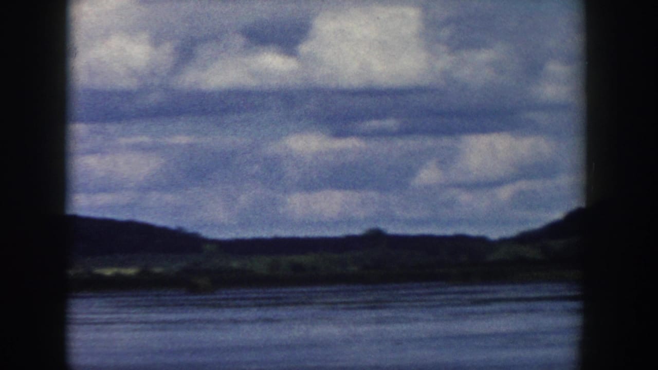 Wisconsin home-movie landscape with a wide water surface, low hills, and heavy clouds, partially obscured by dark frame edges.