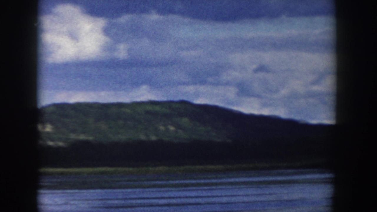Wisconsin 8mm home-movie view of a green hillside across water, with clouds and dark window-like borders in the frame.
