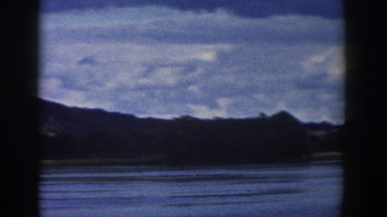 1958 Wisconsin 8mm frame showing a lake, distant dark hills, and partly cloudy sky from a shaded or obstructed vantage point.