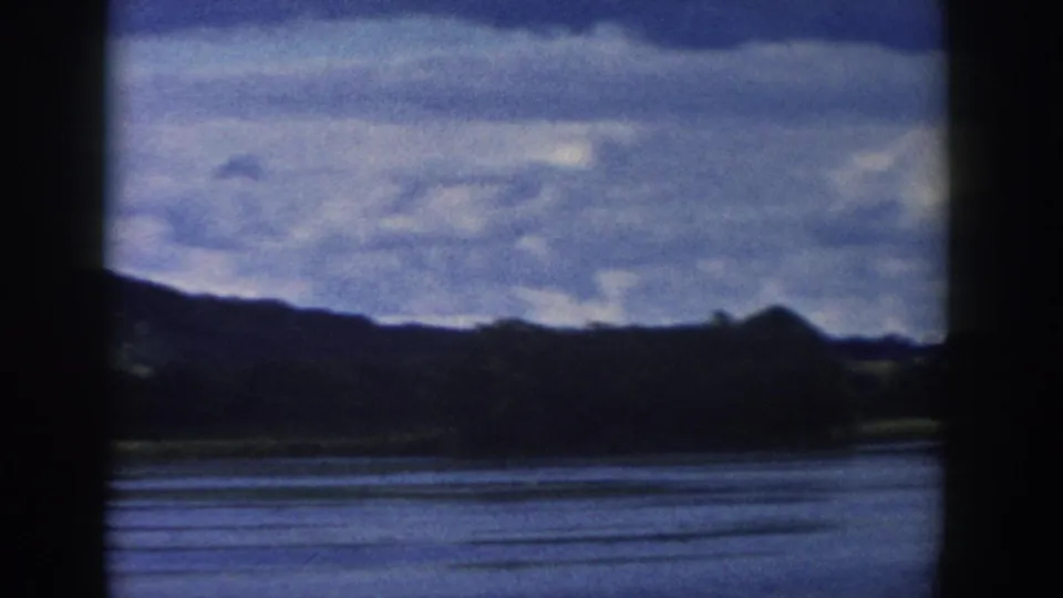 1958 Wisconsin 8mm frame showing a lake, distant dark hills, and partly cloudy sky from a shaded or obstructed vantage point.