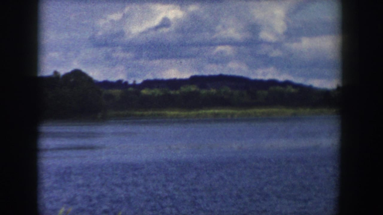 Wide lake surface with low green shoreline, distant hills, and partly sunny clouds.