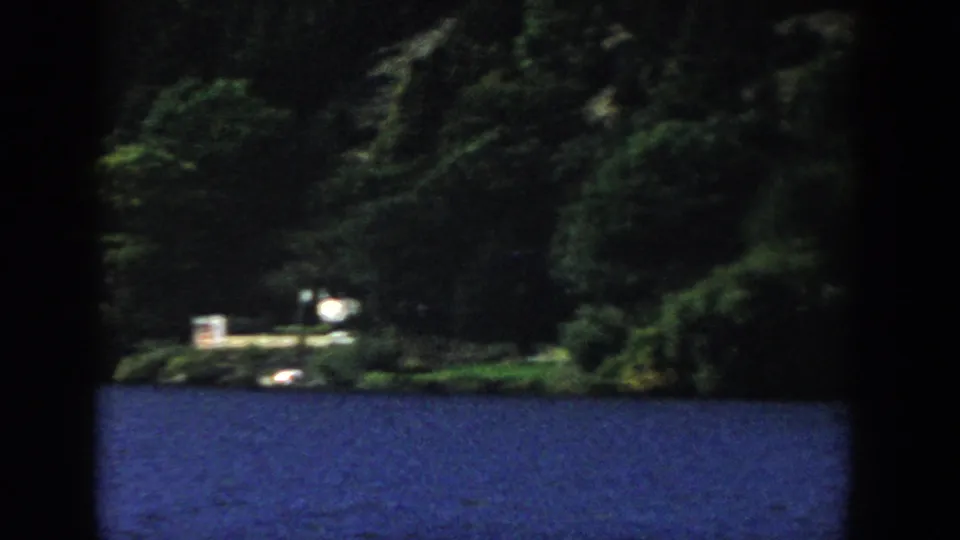1958 Wisconsin 8mm view across blue lake water toward dense trees and small distant shoreline structures.