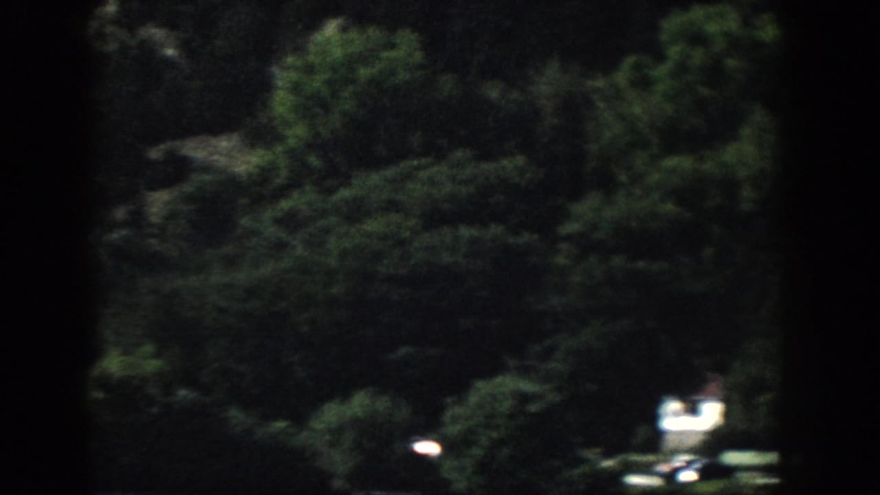 1958 Wisconsin home-movie frame showing a shadowed wooded bank and a small bright vehicle-like shape near the lower edge.