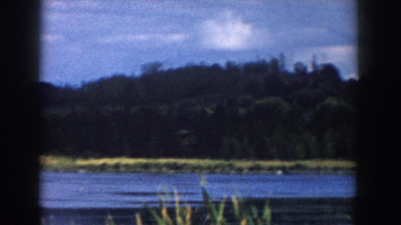 Blue lake, green shoreline, and wooded hill framed by dark vertical bars.