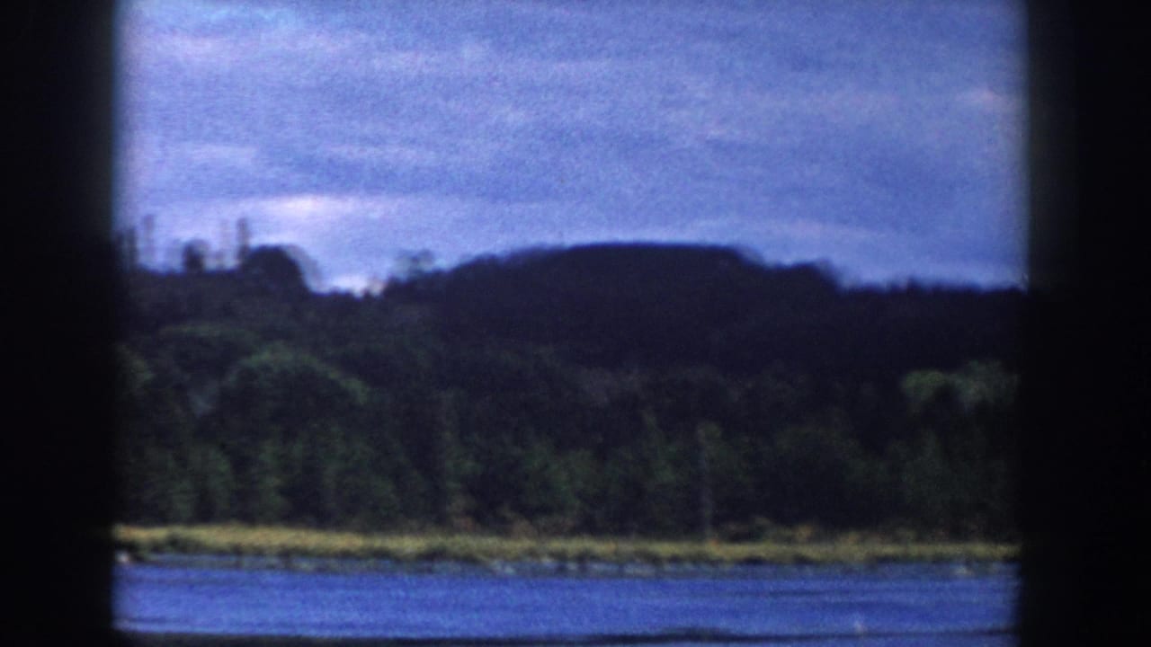 1958 Wisconsin home-movie frame of a cloudy lake view, with water, trees, low hills, and dark window framing across the scene.