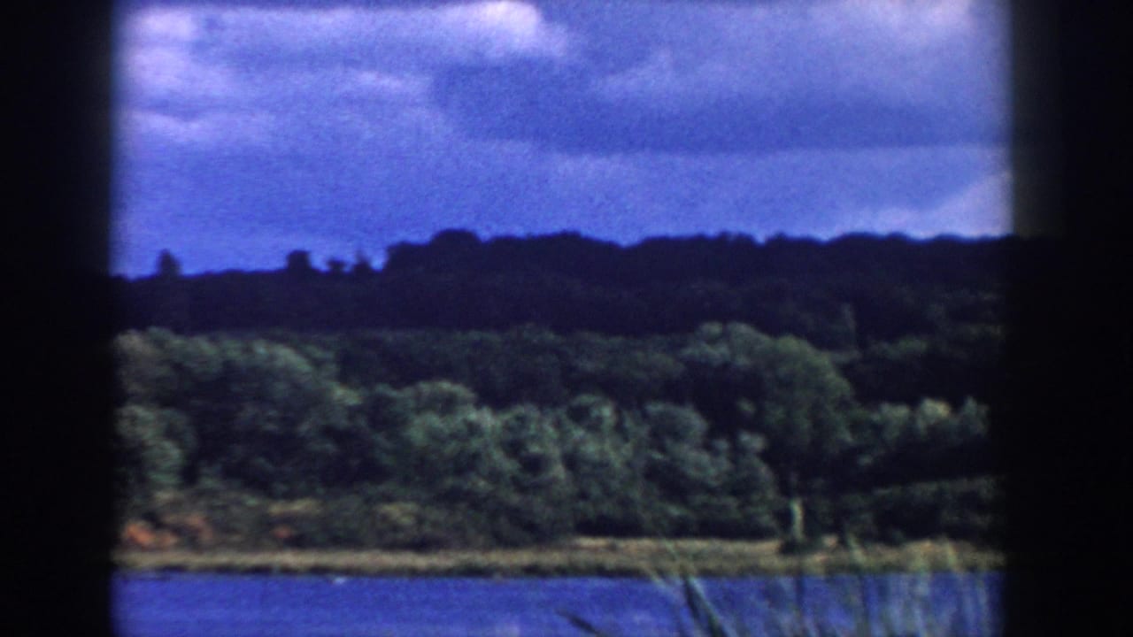 1958 Wisconsin 8mm frame showing a lake, tree-lined shore, cloudy sky, and dark contact-sheet borders.