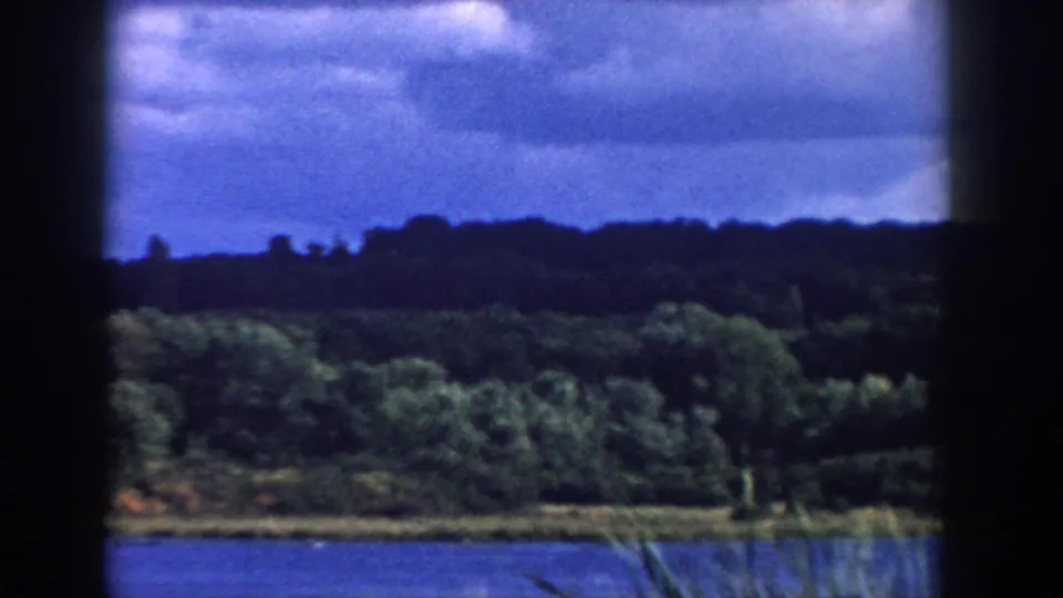 1958 Wisconsin 8mm frame showing a lake, tree-lined shore, cloudy sky, and dark contact-sheet borders.