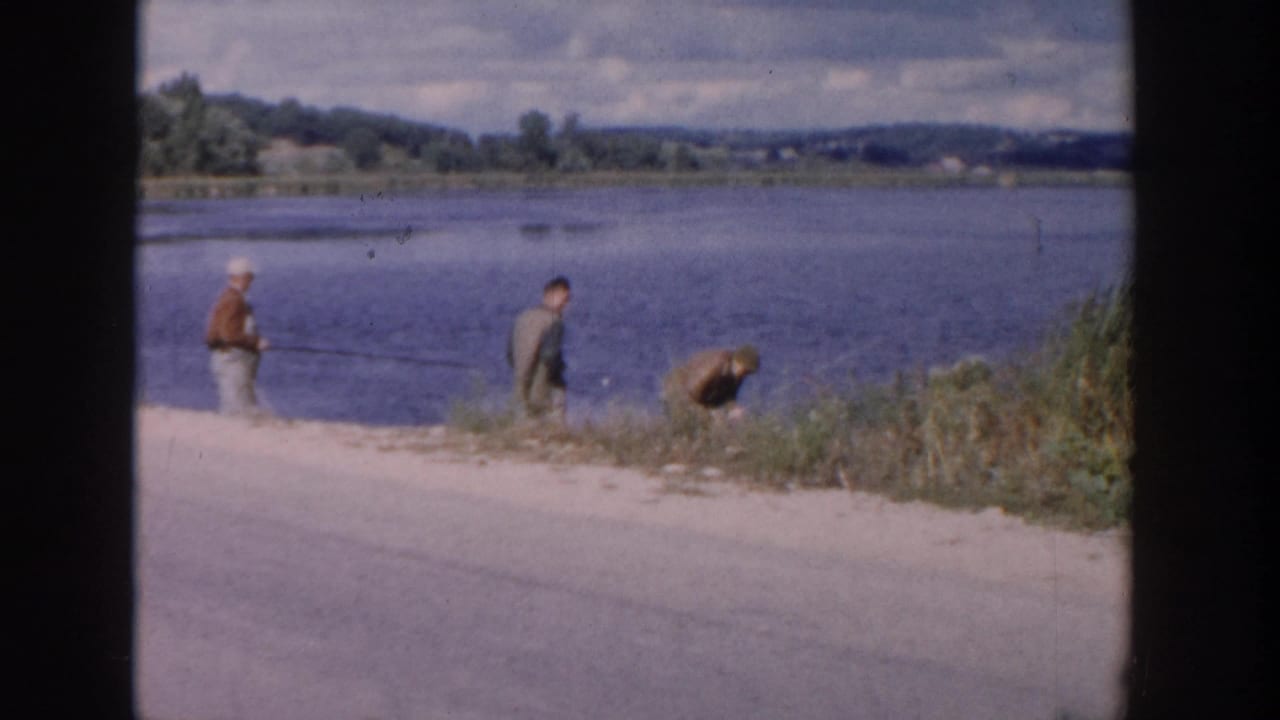 1958 Wisconsin lakeshore scene with boys in casual clothing fishing beside a broad lake and brushy bank.