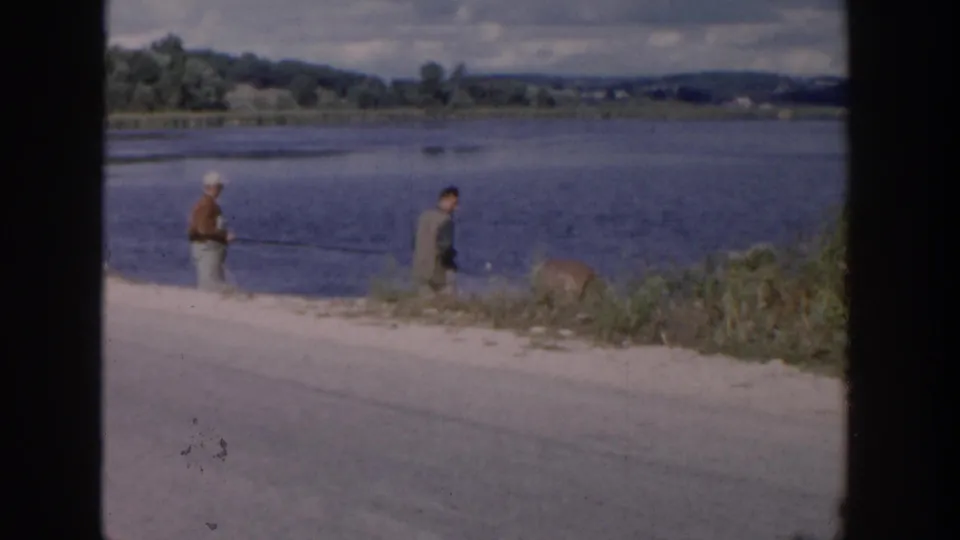Boys continue fishing on a Wisconsin lakeshore, with one figure bending near the brush and others holding rods.