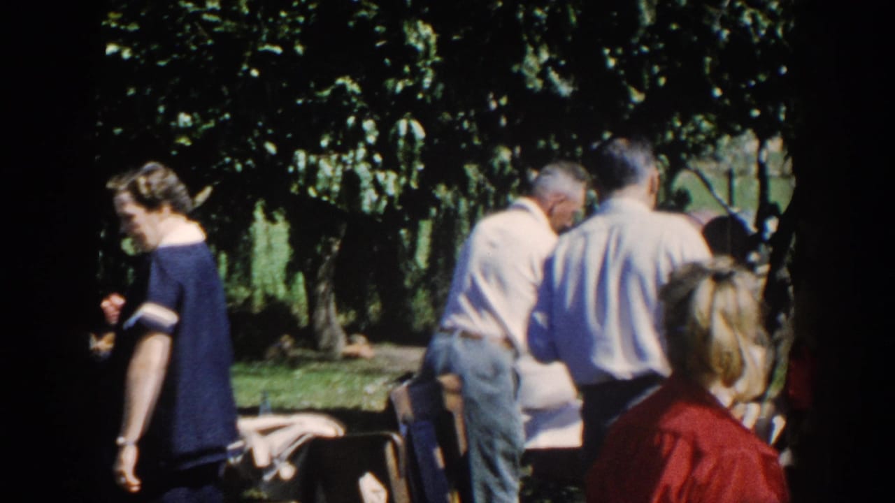 Adults gather in a shaded backyard near a barbecue and serving area.
