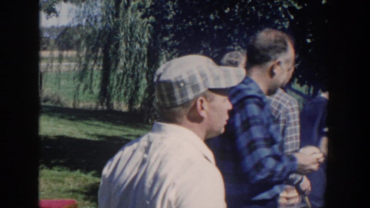 Adults standing on a lawn near a house during an outdoor gathering.