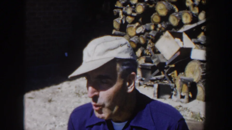 1958 Wisconsin home-movie frame showing the man in profile near stacked firewood, appearing to chew or eat.