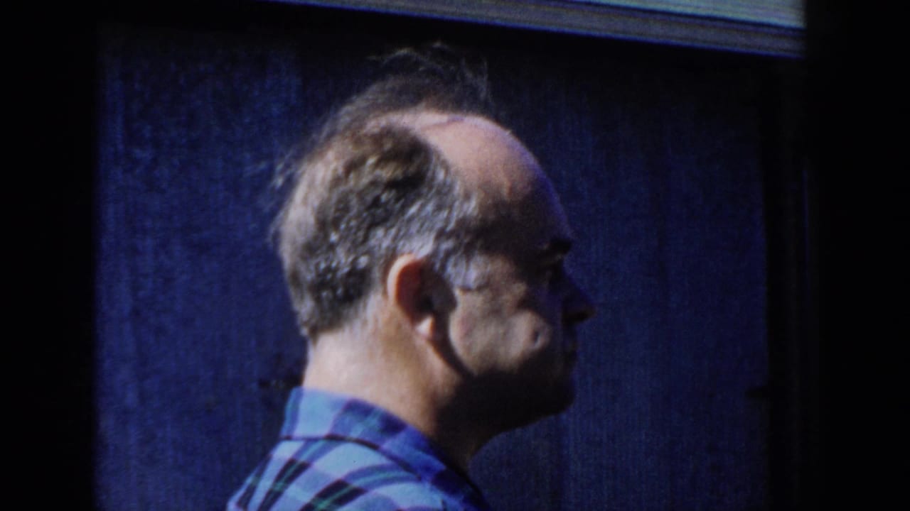 In 1958 Wisconsin home-movie footage, an adult man in a blue plaid shirt is shown in side profile against a dark blue wooden wall.