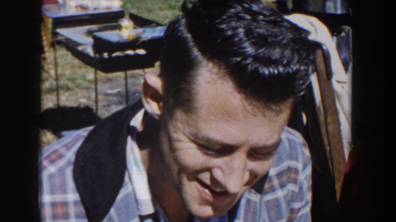 1958 Wisconsin home-movie frame showing a close-up of a young man in a plaid shirt with a dark collar at an outdoor gathering.